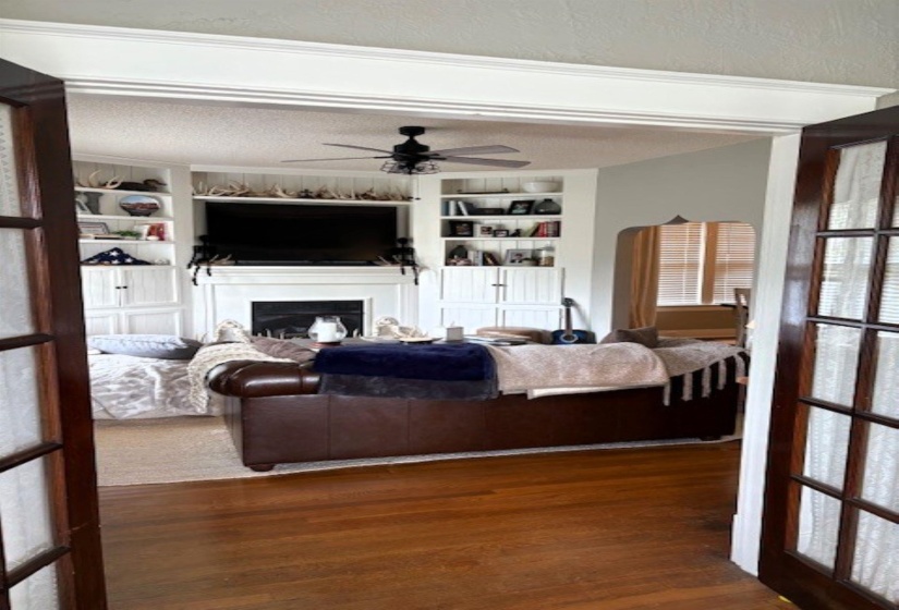 Living room featuring a textured ceiling, a fireplace, dark wood finished floors, built in shelves, and ceiling fan