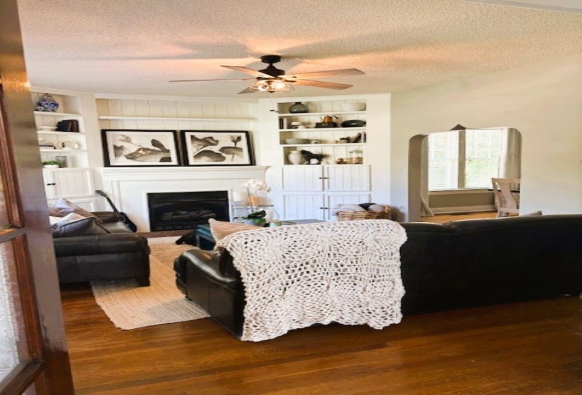 Living area featuring a textured ceiling, a ceiling fan, built in shelves, dark wood finished floors, and a fireplace