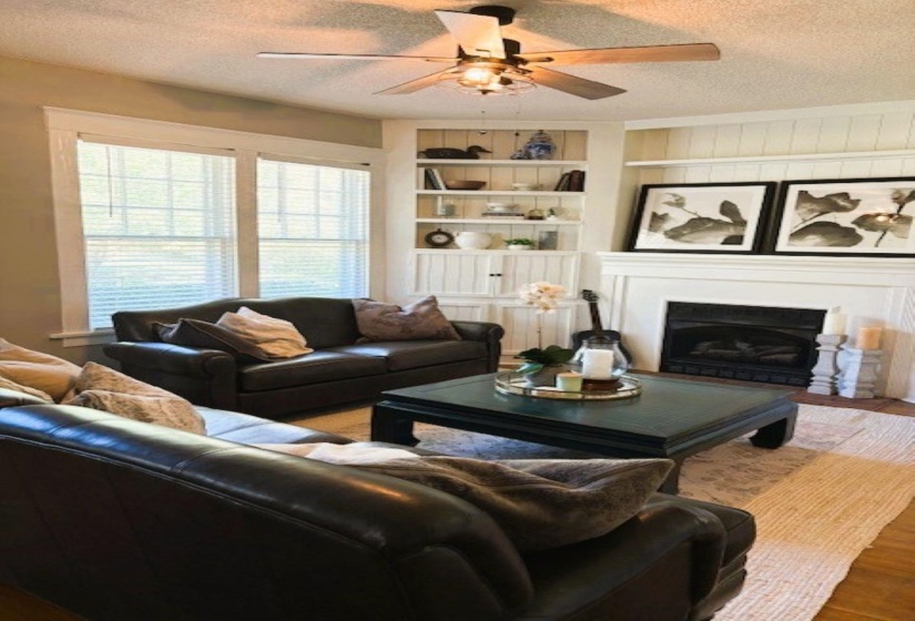 Living room with a textured ceiling, a fireplace, ceiling fan, built in shelves, and wood finished floors