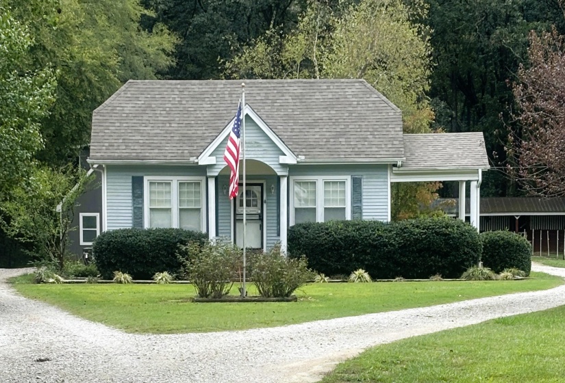 View of front facade featuring a front yard, roof with shingles, and gravel driveway