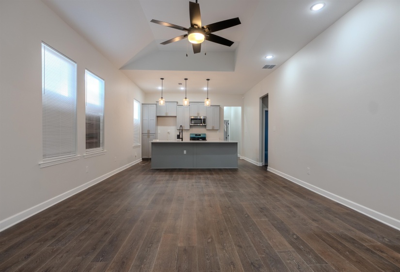 Kitchen featuring dark hardwood / wood-style floors, appliances with stainless steel finishes, a kitchen island with sink, and decorative light fixtures