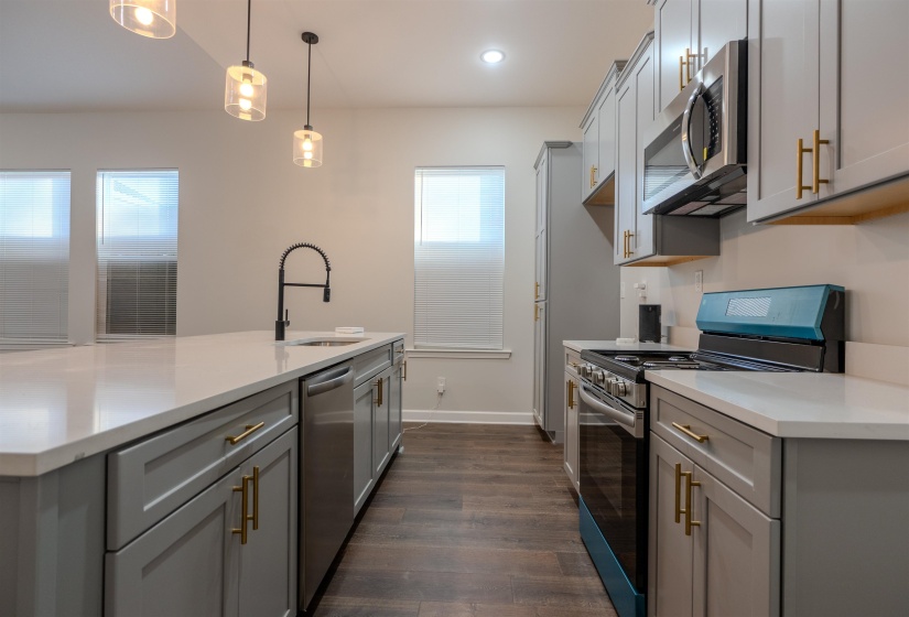 Kitchen featuring an island with sink, gray cabinetry, stainless steel appliances, sink, and pendant lighting