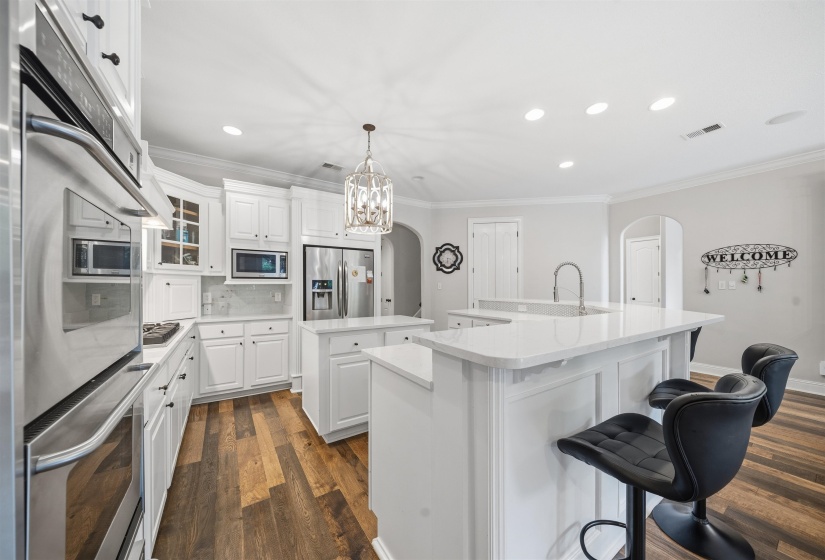 Expansive kitchen featuring white cabinetry, wood-finish flooring, a double wall oven, and a large central island with a built-in sink