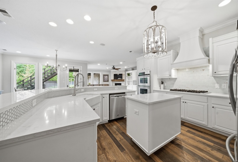 White kitchen featuring wood-finish flooring, white cabinetry, integrated double ovens, and a large decorative light fixture