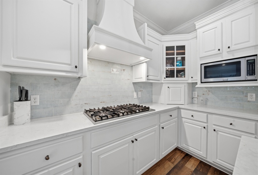 Bright kitchen featuring white cabinetry, a built-in microwave, a gas cooktop, light-toned countertops, and wood-finish flooring