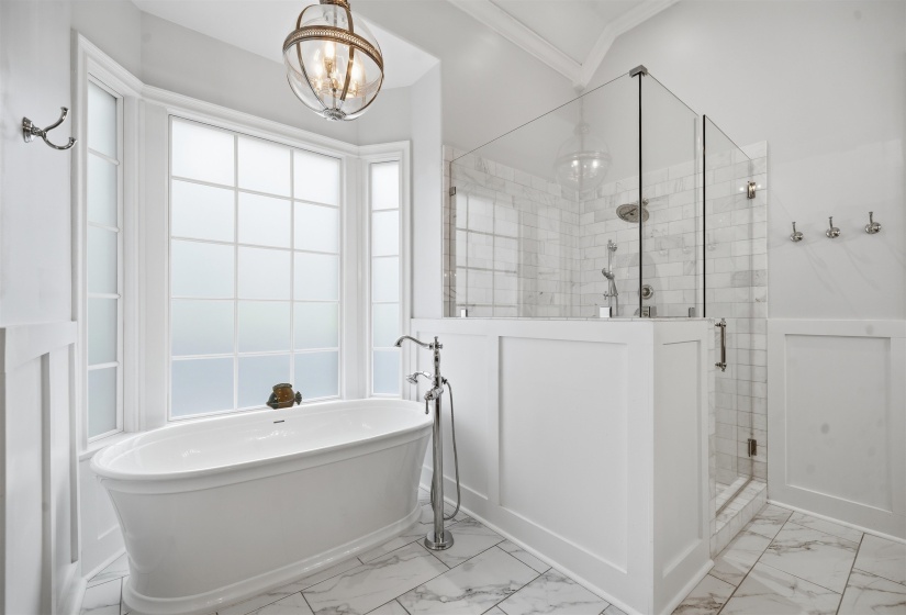 Freestanding soaking tub with a floor-mounted faucet, bay window with frosted glass, and a walk-in shower with clear glass enclosure