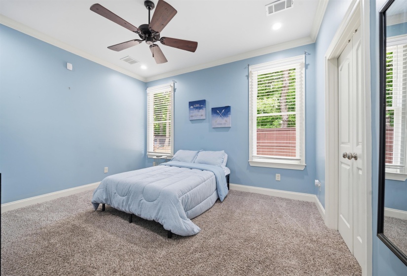 Carpeted interior with crown molding, two windows with blinds, a ceiling fan, and a built-in closet with bifold doors