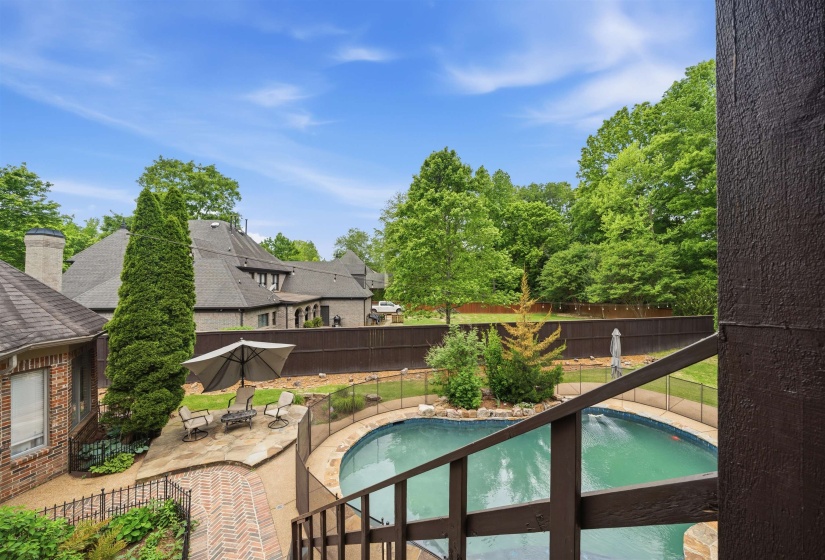 Gated freeform swimming pool with a surrounding patio, brick paver walkway, and mature landscaping