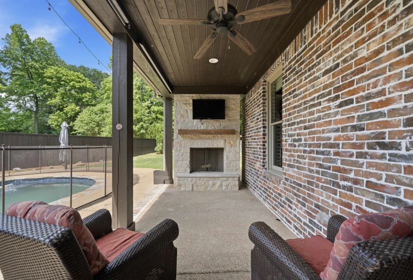 Covered patio featuring a stone fireplace with a wood-finish mantel, wood-plank ceiling, and a ceiling fan