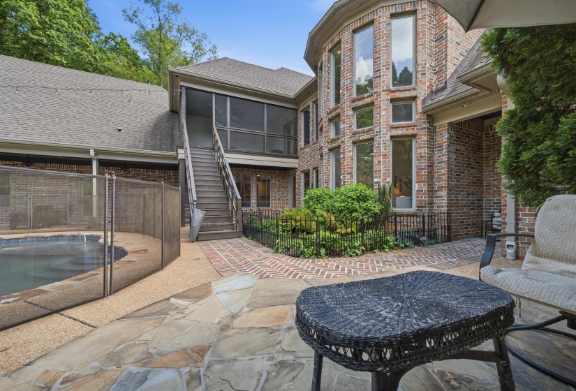 Stone patio with a private pool, screened-in porch with exterior staircase, and a multistory brick exterior with multiple windows