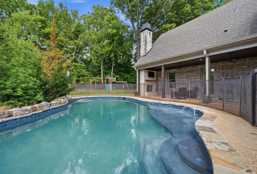 Freeform swimming pool with integrated steps, stone coping, and surrounding safety fencing