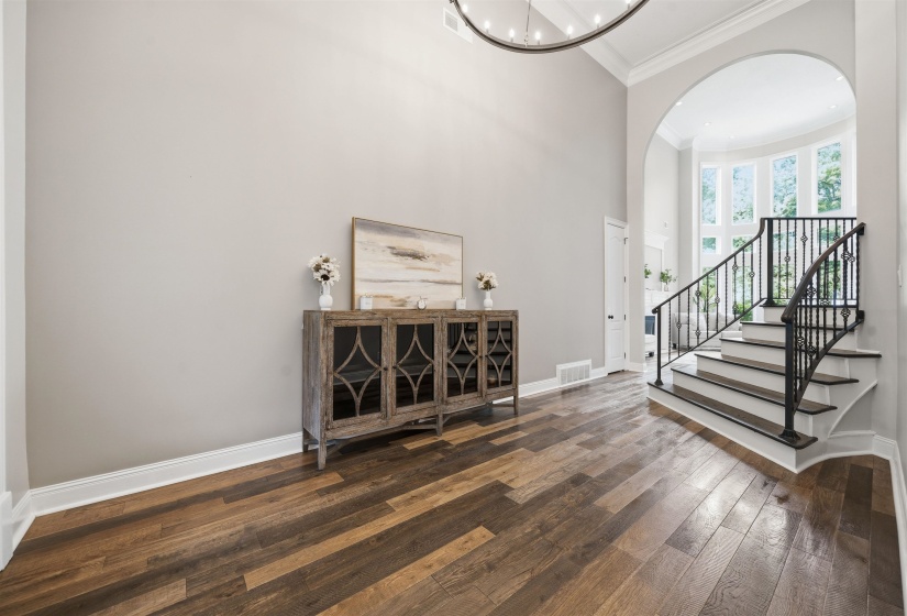 Two-story foyer featuring wide-plank wood-finish flooring, a custom iron staircase, and a large arched entryway with a semicircular window wall
