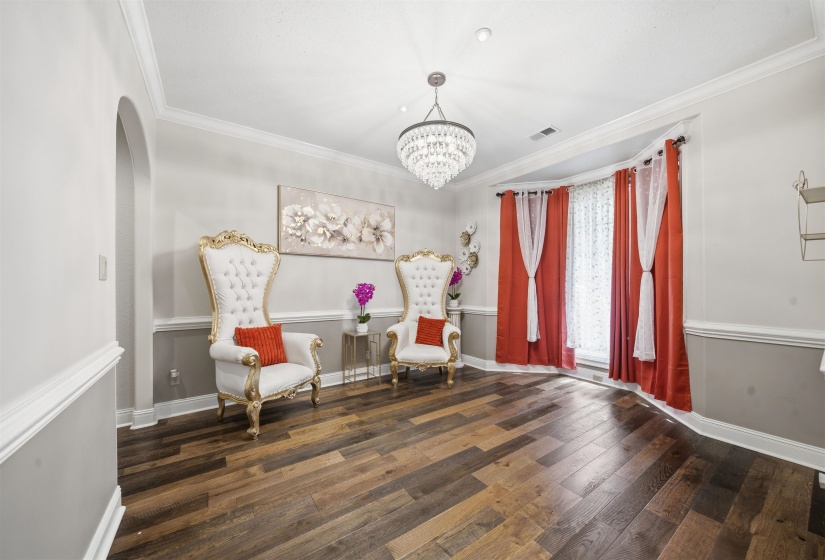 Room featuring wood-finish flooring, a tiered crystal chandelier, an arched doorway, and bay windows with red drapery