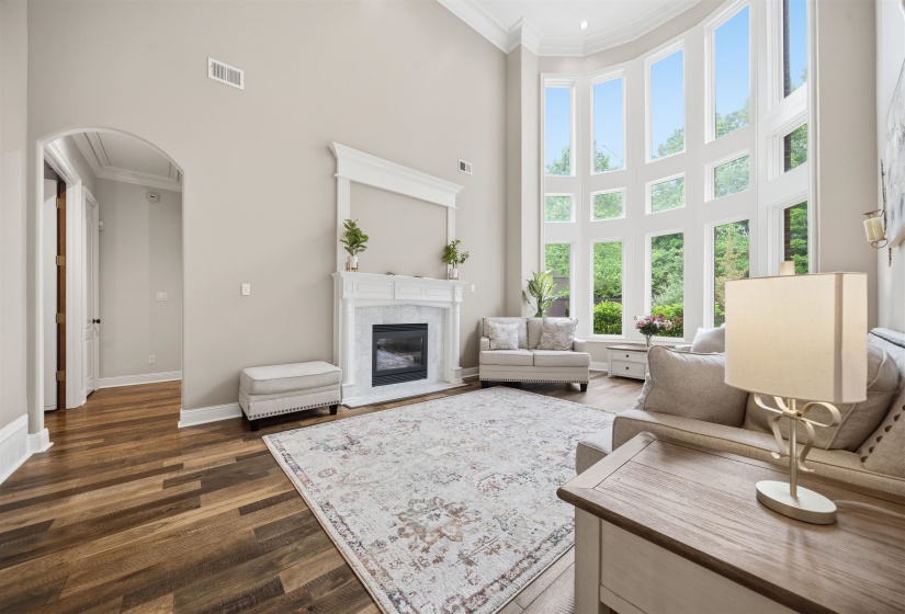 Two-story living area with expansive window wall, wood-finish flooring, and a fireplace with a stone surround