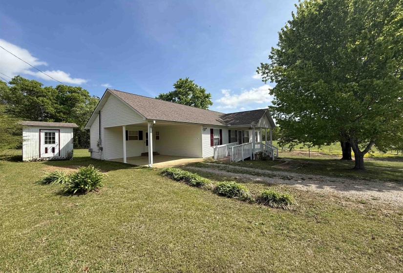 View of property exterior with an attached carport, a yard, driveway, and a storage unit