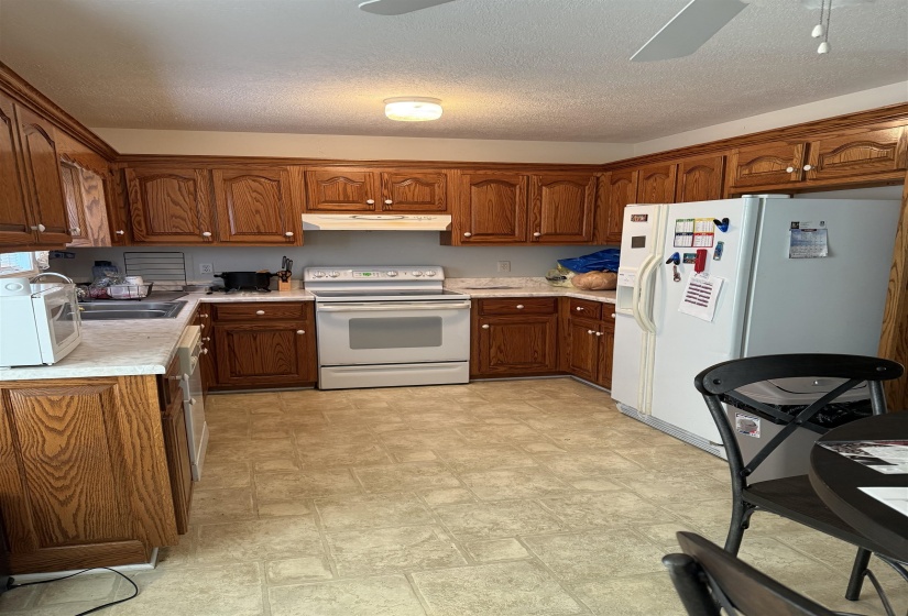 Kitchen featuring a ceiling fan, light countertops, white appliances, a textured ceiling, and wood finish cabinets