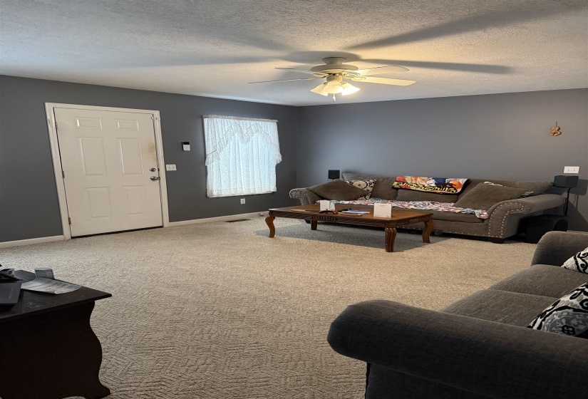 Carpeted living room with a ceiling fan and a textured ceiling
