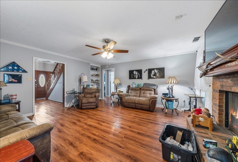 Living room featuring wood finished floors, a brick fireplace, a textured ceiling, ceiling fan, and crown molding