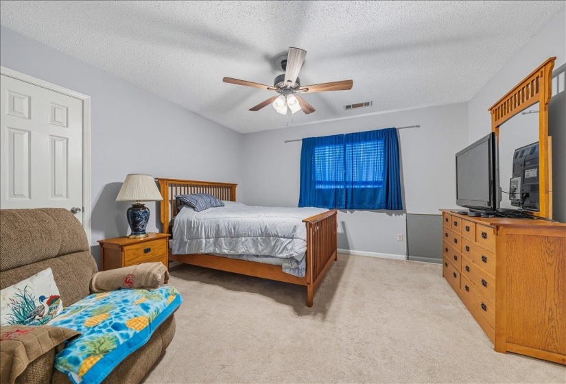 Bedroom with a textured ceiling, light colored carpet, and a ceiling fan