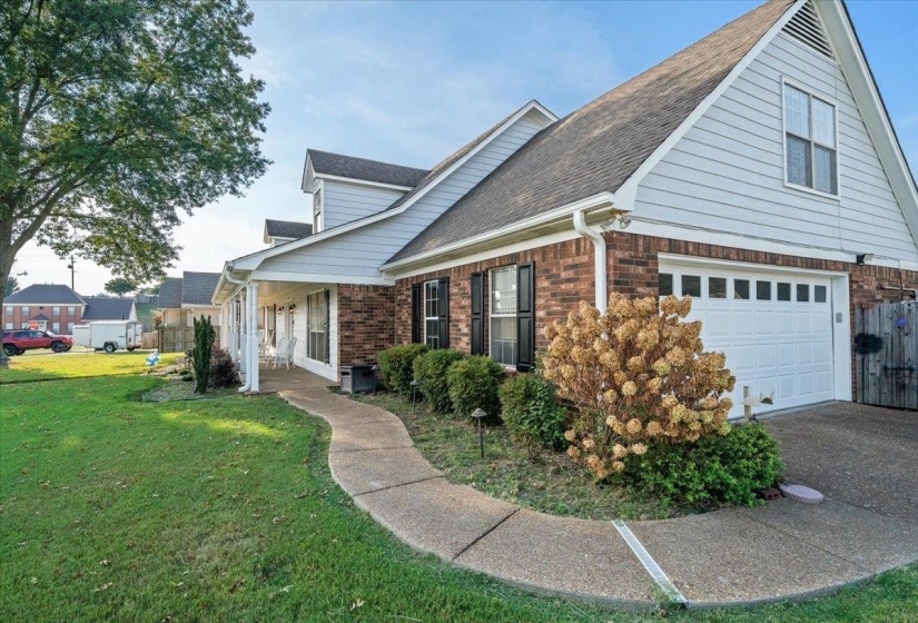 View of side of home with brick siding, roof with shingles, driveway, and covered porch