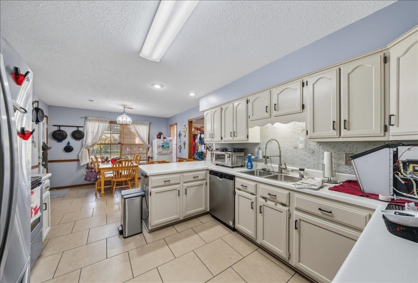 Kitchen featuring light countertops, a peninsula, stainless steel appliances, light tile patterned flooring, and a textured ceiling