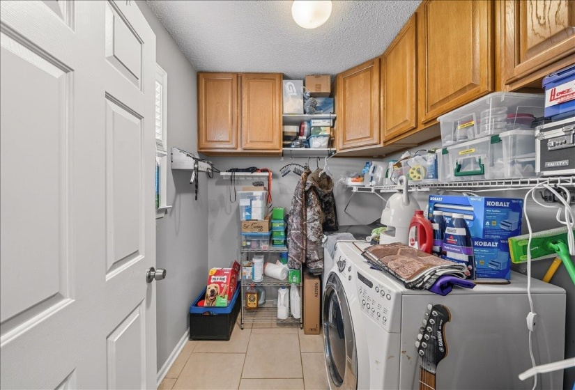 Laundry area with a textured ceiling, washing machine and dryer, cabinet space, and light tile patterned floors
