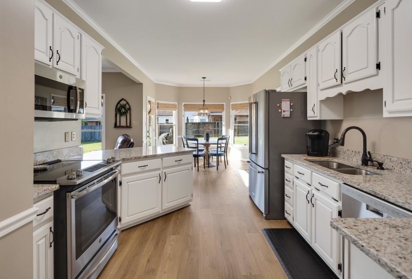 Kitchen featuring stainless steel appliances, light stone counters, a peninsula, white cabinetry, and ornamental molding