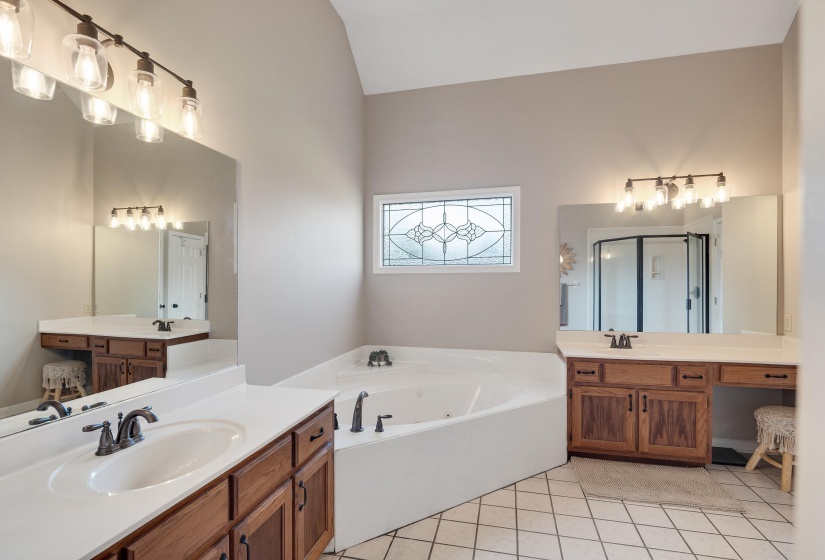 Bathroom with two vanities, a jetted tub, light tile patterned flooring, and vaulted ceiling