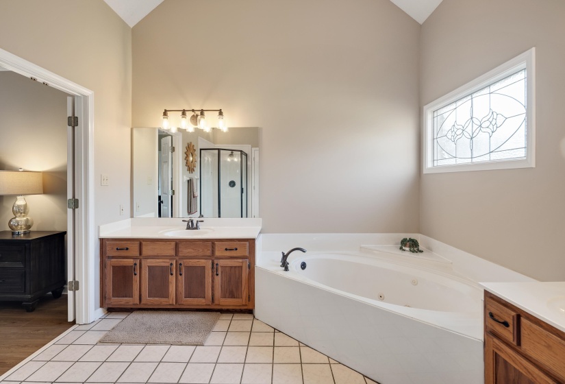 Bathroom with vanity, a tub with jets, light tile patterned flooring, a stall shower, and lofted ceiling