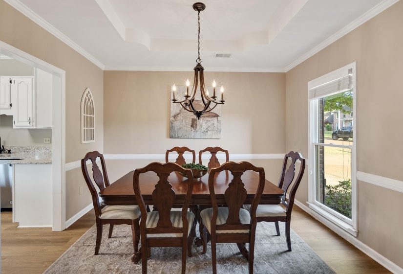 Dining room with light wood-style flooring, ornamental molding, hanging lights, and a raised ceiling
