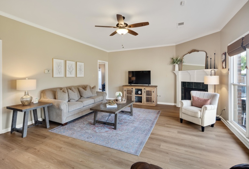 Living area featuring a ceiling fan, light wood-style flooring, a tiled fireplace, and crown molding