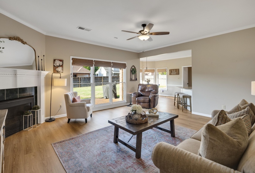 Living area featuring light wood-type flooring, a tiled fireplace, ceiling fan, and ornamental molding