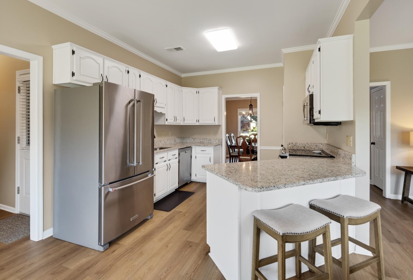 Kitchen with stainless steel appliances, a peninsula, a breakfast bar, light wood-style floors, and white cabinets