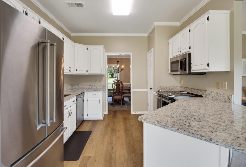 Kitchen with stainless steel appliances, ornamental molding, light stone countertops, white cabinets, and light wood-type flooring
