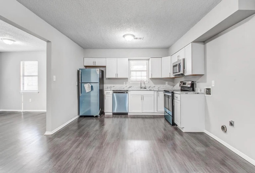 Kitchen with stainless steel appliances, light countertops, white cabinets, a textured ceiling, and dark wood finished floors