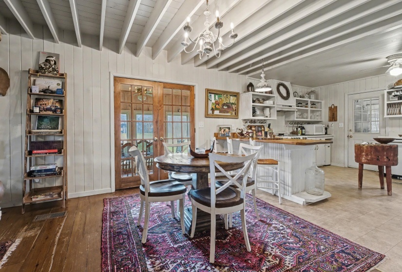 Dining room with wood walls, a ceiling fan, beamed ceiling, french doors, and suspended lighting