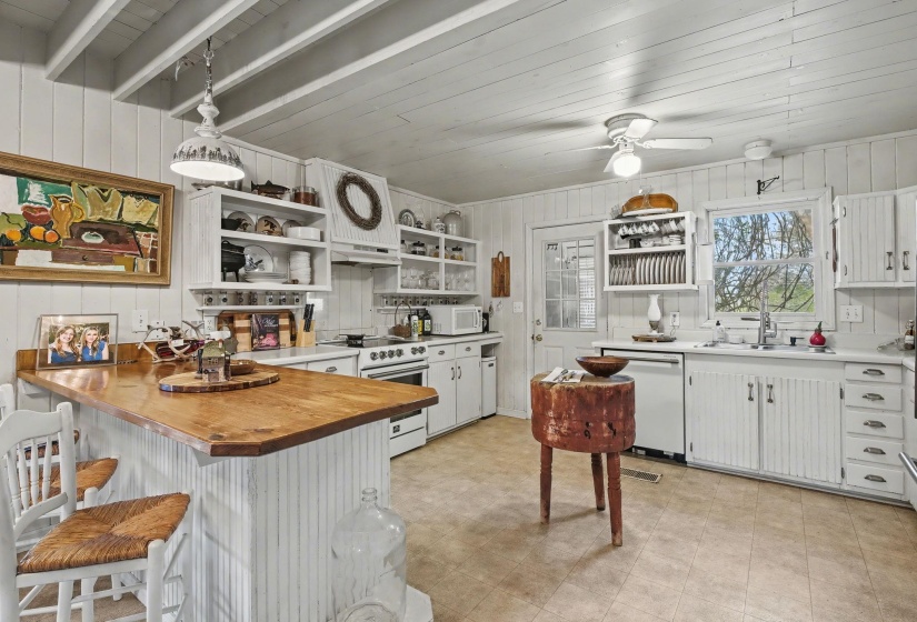 Kitchen with white cabinets, a peninsula, white appliances, pendant lighting, and wooden walls