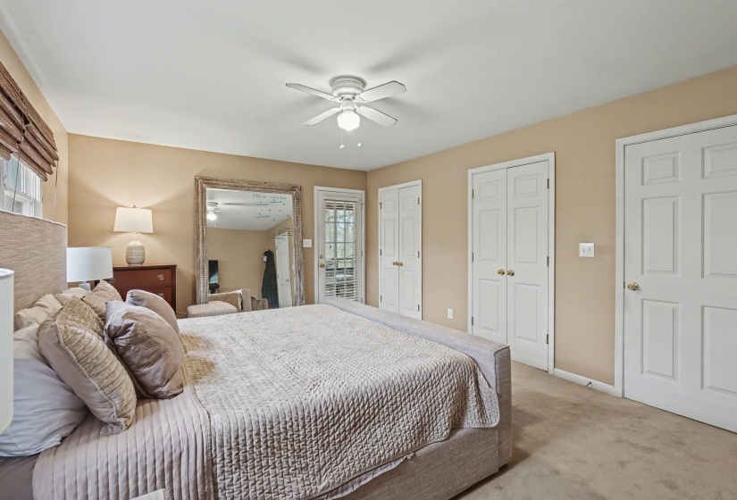 Carpeted bedroom with two closets, ceiling fan, and multiple windows