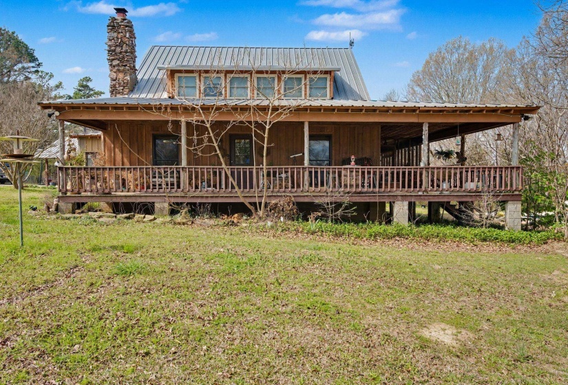Rear view of house with board and batten siding, covered porch, a lawn, a chimney, and a metal roof