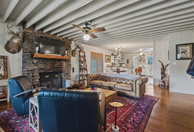 Living room featuring wooden walls, suspended lighting, a ceiling fan, dark wood-type flooring, and a fireplace