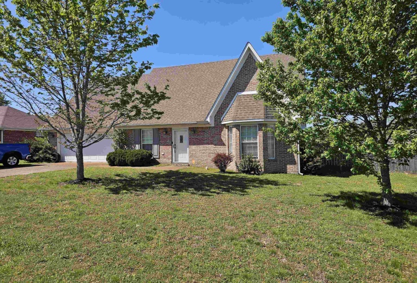 View of front of property with brick siding, roof with shingles, a front yard, and an attached garage