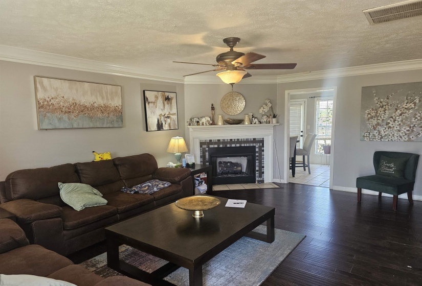 Living room featuring a ceiling fan, a textured ceiling, wood finished floors, crown molding, and a fireplace