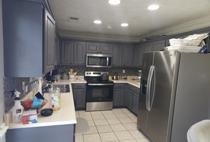 Kitchen featuring gray cabinets, stainless steel appliances, light countertops, backsplash, and ornamental molding