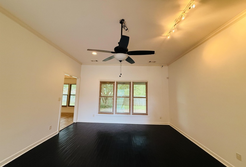 Empty room with crown molding, a ceiling fan, dark wood-type flooring, and track lighting