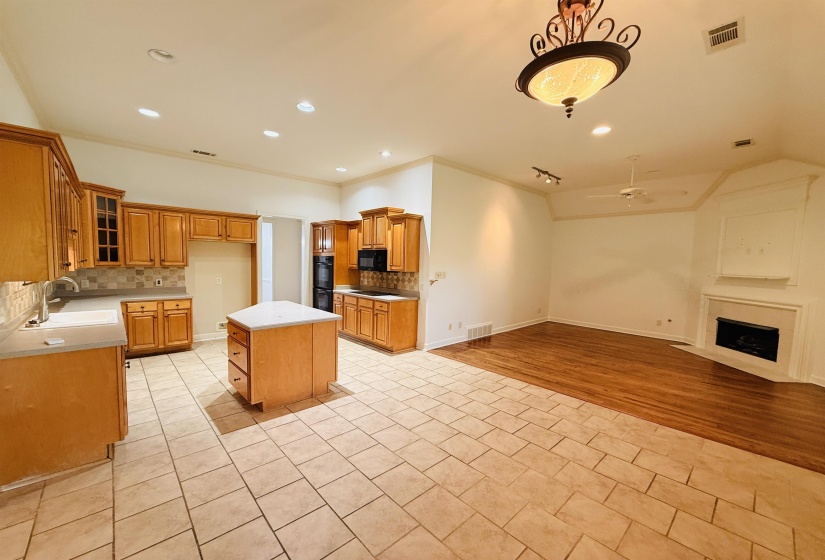 Kitchen featuring a kitchen island, light tile patterned flooring, open floor plan, wood finish cabinetry, and crown molding