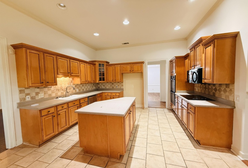 Kitchen featuring wood finish cabinets, a kitchen island, light tile patterned flooring, light countertops, and crown molding