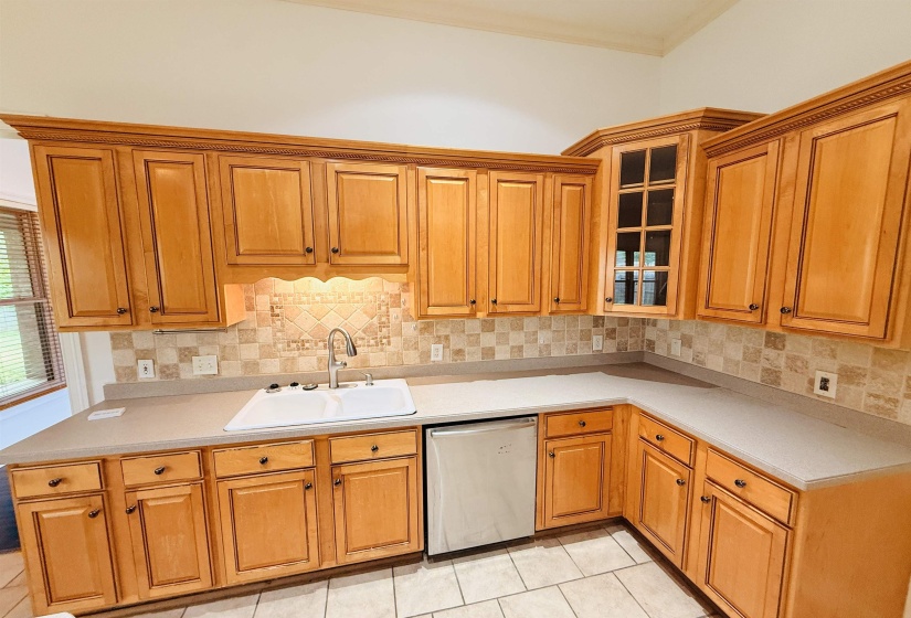 Kitchen with dishwasher, glass insert cabinets, light countertops, wood finish cabinetry, and backsplash