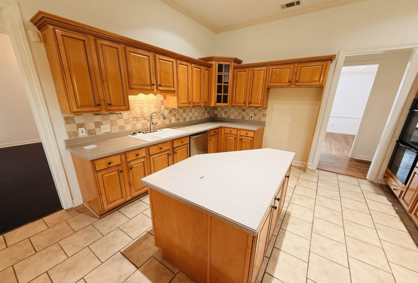 Kitchen featuring wood finish cabinetry, decorative backsplash, light countertops, a kitchen island, and crown molding