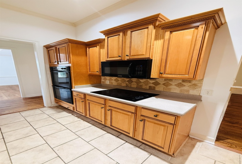 Kitchen with light countertops, light tile patterned flooring, backsplash, black appliances, and crown molding