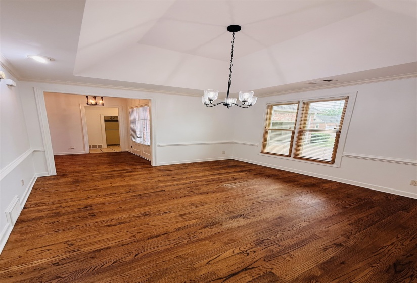 Unfurnished dining area featuring hanging lights, dark wood-type flooring, ornamental molding, and a raised ceiling